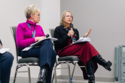 125. Lisa Levin speaks while gesturing with her hand, with Krista Carr seated next to her