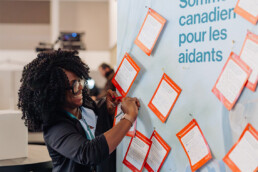 Afolasade Fakolade épingle sa carte postale du Sommet au mur de cartes postales remplies des espoirs des participants pour une stratégie nationale sur la prestation de soins