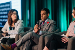 Dr. Samir Sinha speaking on stage during a session on homecare, seated alongside Dr. Pam Orzeck and Christine Kelly, who is slightly out of frame