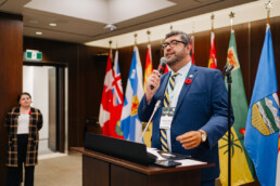 CCCE’s James Janeiro gives a welcome speech behind the podium at the reception. Behind him are a collection of standing flags