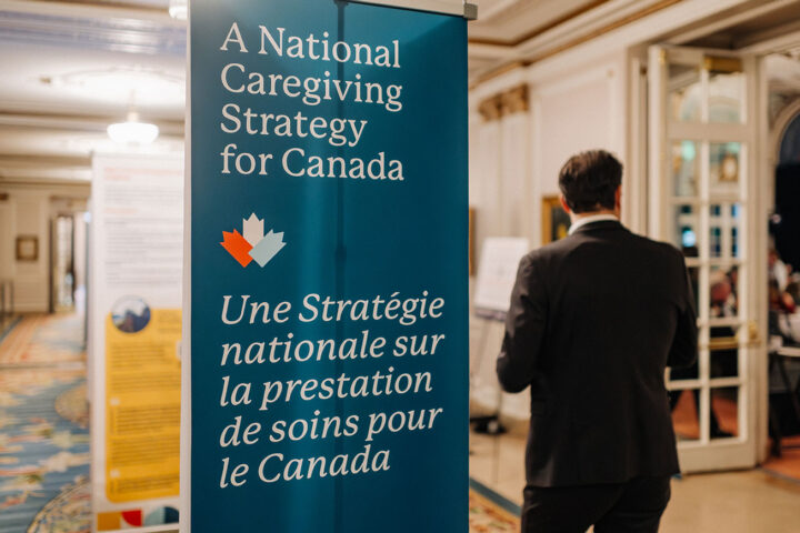 A man in a suit walks past a banner that reads “A National Caregiving Strategy for Canada” in English in French.
