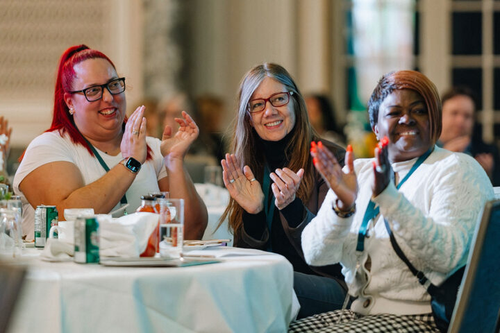 Sue Hutton, Claudiane Coutu Arbour and Fredrica Pottinger seated at a round table and clapping
