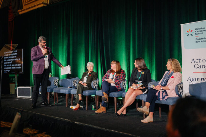 James Janeiro stands on stage during the advocacy workshop, gesturing towards his fellow speakers who are seated in blue armchairs