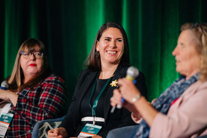 Heather Mulligan smiles on stage, with fellow speakers from the advocacy workshop blurred on either side of her