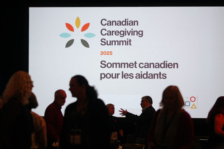 Silhouettes of attendees walking past a giant white screen with the Canadian Caregiving Summit logo