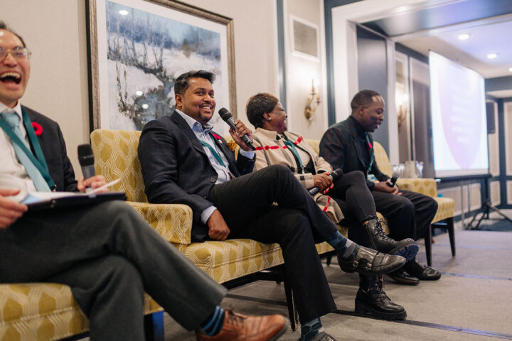 Panelists at the care delivery session sharing a moment of laughter, with Kumaran Nadesan in focus holding the microphone.