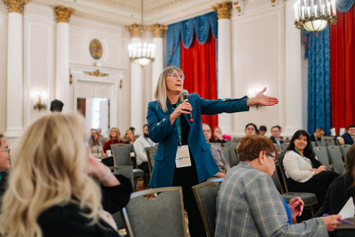 CCCE advisory council member Barb McLean stands and gestures while asking a question at a session.