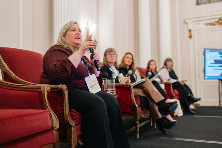 Aimee Foreman from Caregivers New Brunswick speaks on stage, with fellow panelists from the East Coast panel seated next to her
