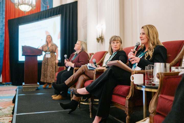 Speakers from the East Coast panel seated on stage, with Kimberly Leonard from SeniorsNL holding the microphone.