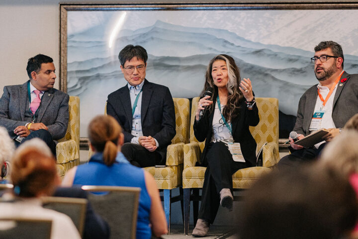 Ito Peng gestures while speaking on stage at the Care Insurance panel, with fellow panelists seated next to her
