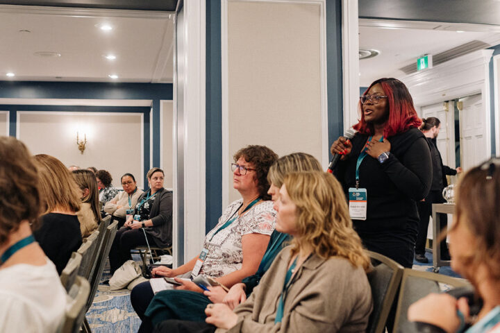 An audience member with long black hair with red highlights asks a question during a panel