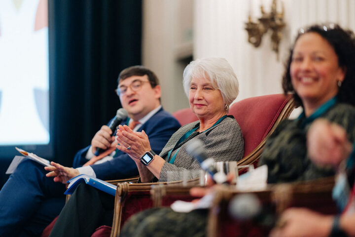 Pamela Barkhouse claps during a moment in the panel on financial security, with fellow panelists blurred on either side.