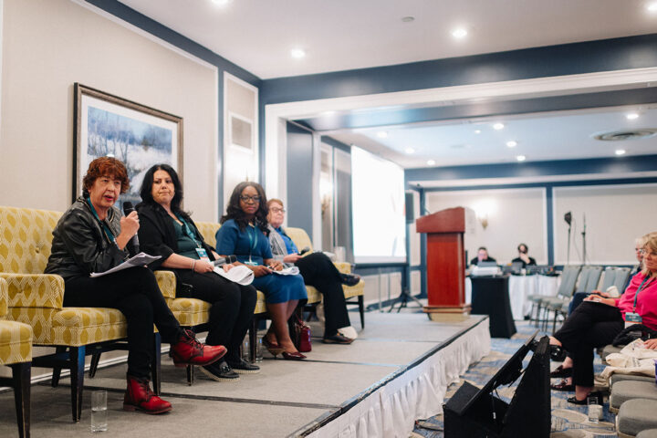 Speakers from the panel on double duty caregivers seated on stage, with Bharati Sethi in focus.