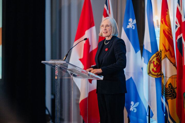 Minister Patty Hajdu speaking on stage at the parliamentary reception against a background of hanging flags.