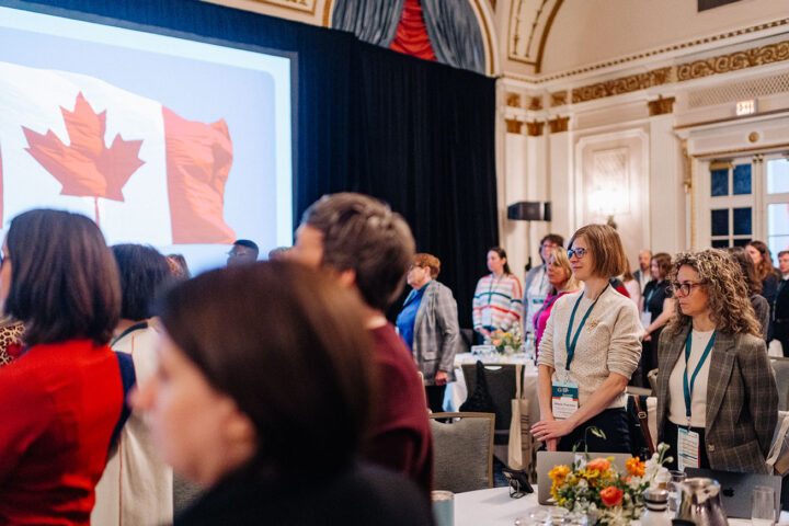 Attendees standing for the national anthem, with a screen displaying the Canadian flag.