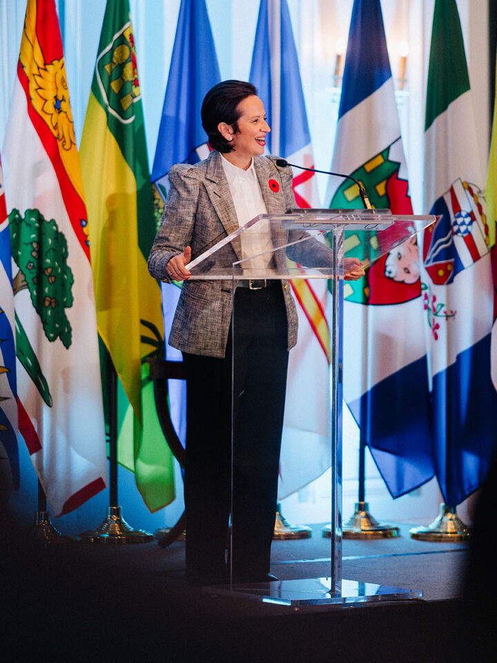 MP Melissa Lantsman speaks on stage at the parliamentary reception, against a background of hanging flags.