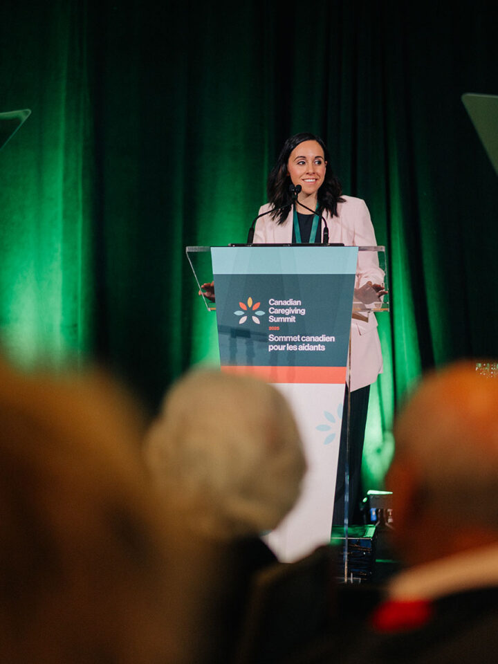 Summit emcee Stephanie Muskat stands at the podium, addressing attendees.