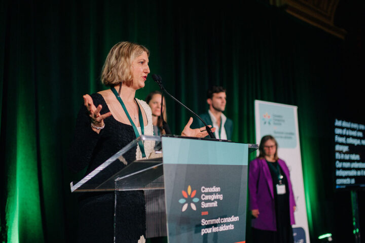 Lina Caschetto speaks at the podium, with her siblings on stage in the background