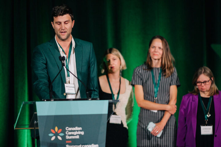 Joel Caschetto speaks at the podium, with his siblings on stage in the background