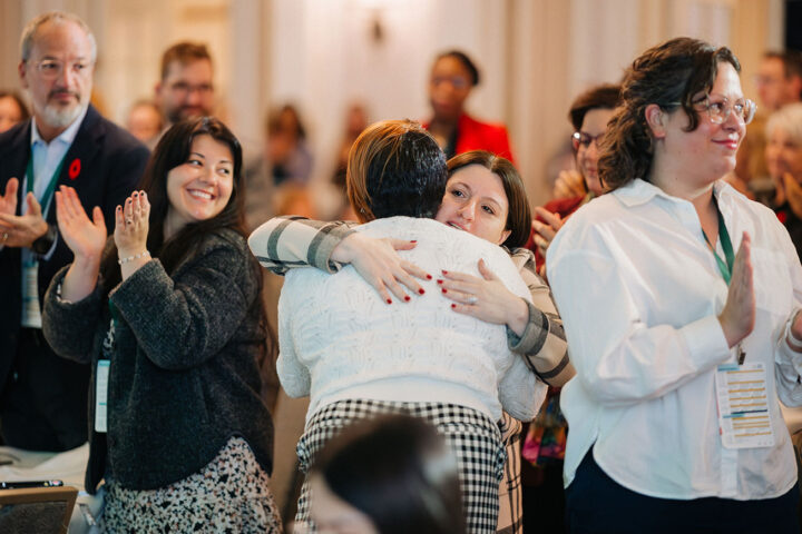 CCCE's Liv Mendelsohn and Fredrica Pottinger share a hug, surrounded by other applauding attendees
