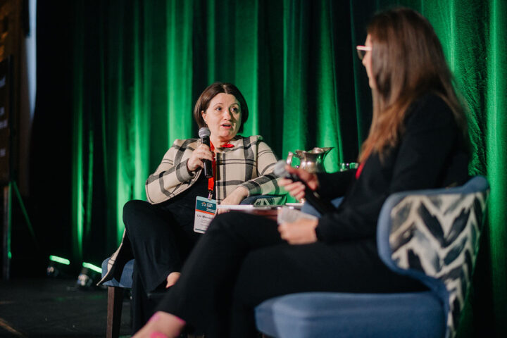 CCCE's Liv Mendelsohn sits on stage with microphone in hand, next to Stephanie McLean, Secretary of State for Seniors